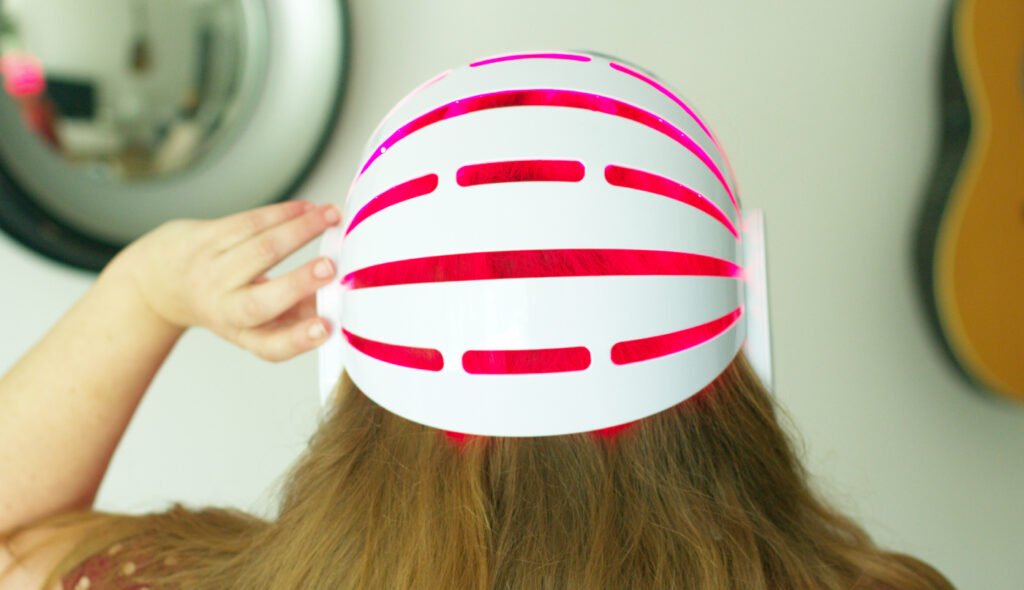 Personne vue de dos portant un casque LED rouge pour le soin des cheveux