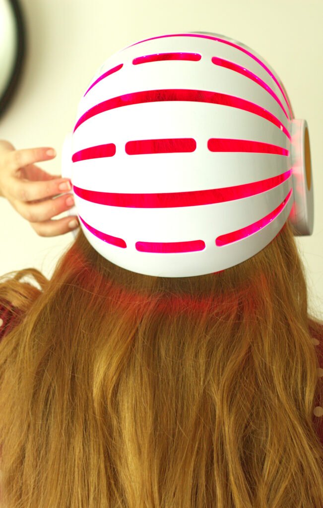 Personne vue de dos portant un casque LED rouge pour le soin des cheveux